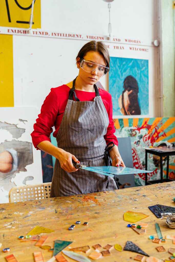 A woman in a studio working on stained glass art, showcasing creativity and skill in a vibrant workshop.
